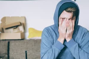A hooded figure is sat on a sofa with head in hands, supressing anger. Anger management can help improve relationships. Image by Christian Urfurt, Unsplash.
