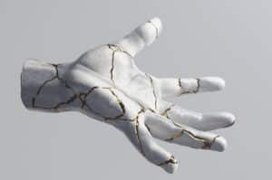 Image shows a Kintsugi, a once broken hand sculpture glued back together with gold. Used to illustrate reducing hurt in relationships. By Simon Lee, Unsplash.